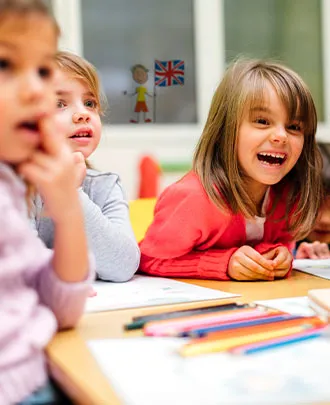 3 élèves de maternelle qui rigolent autour d'une table lors d'un cours d'anglais avec Institut Molière